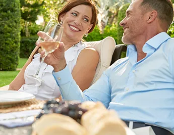 A smiling man and a woman at an outdoor table with food and wine